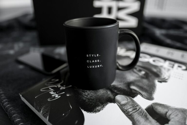 A stylish black mug with text sits on a luxury magazine, presenting an elegant and modern lifestyle setting indoors.